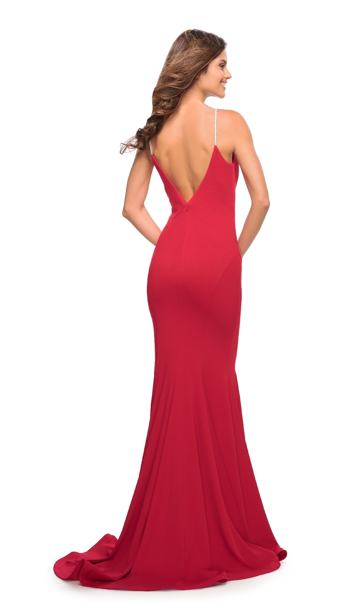 Woman in a floor-length, sleeveless La Femme Long Jersey Mermaid Prom Dress 30785 with a deep V-back, standing and looking over her shoulder against a white background.